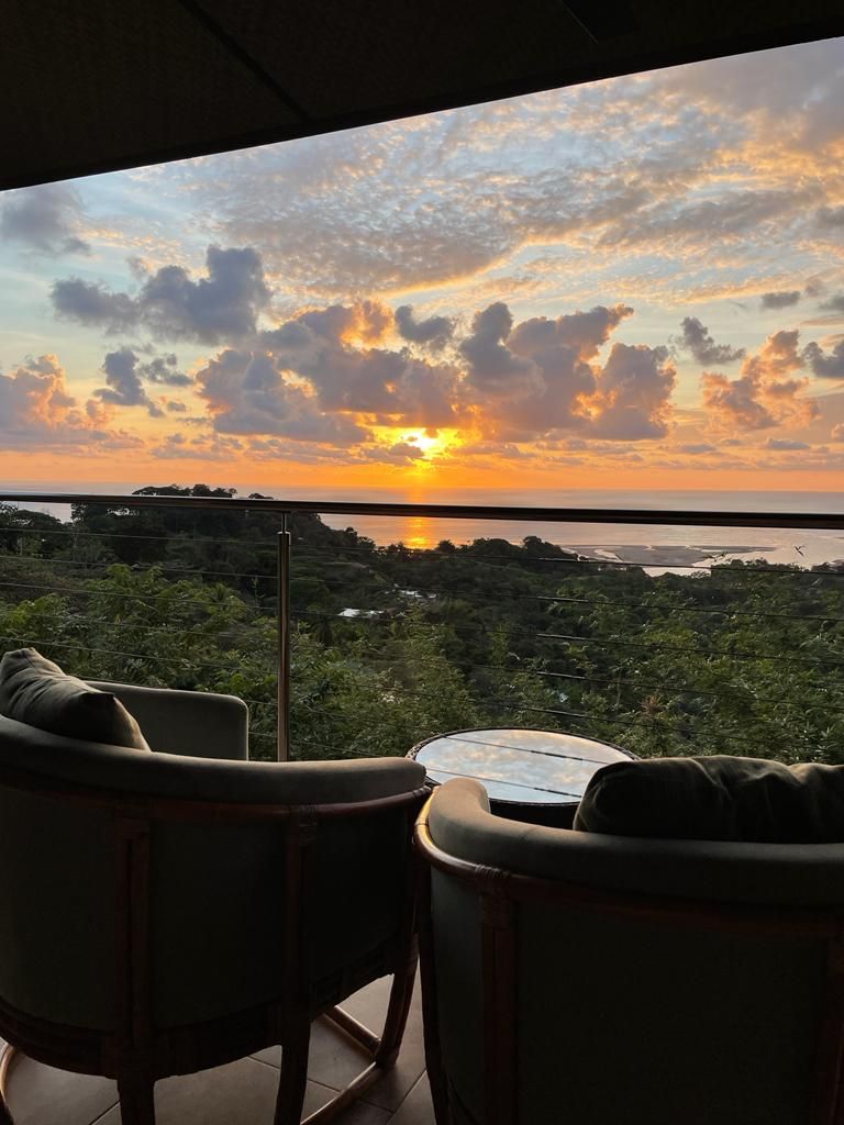 Two chairs are sitting on a balcony overlooking a sunset.