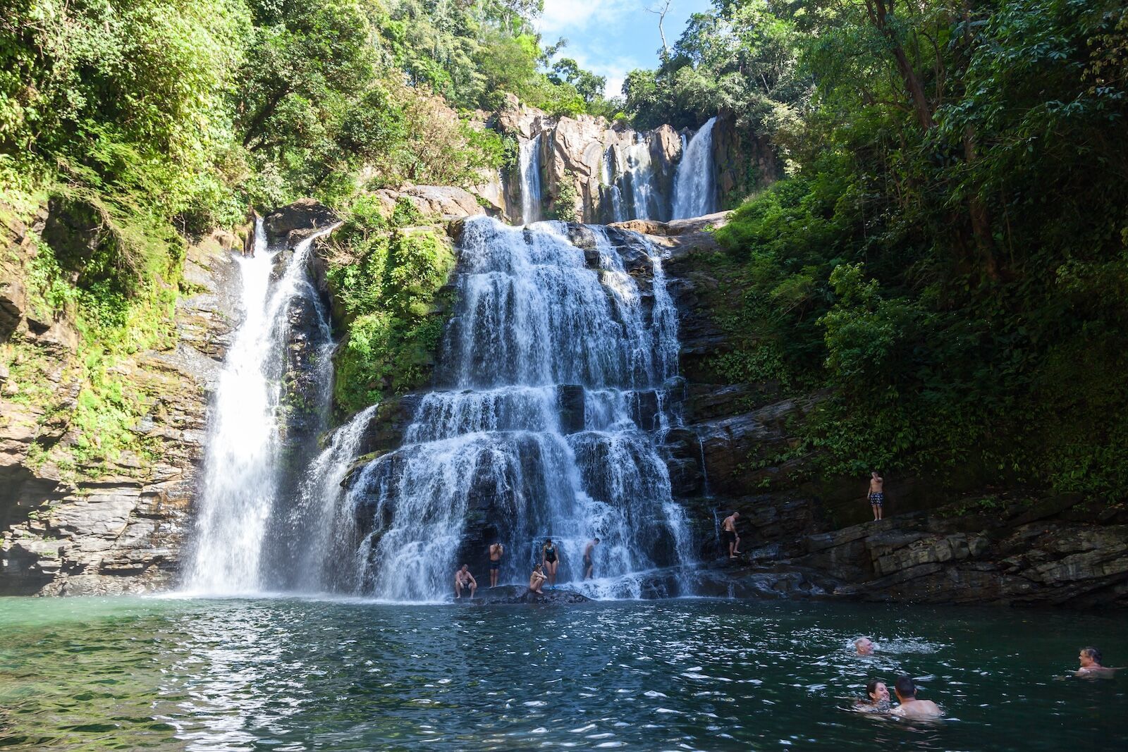 A waterfall in the middle of a forest with people swimming in it