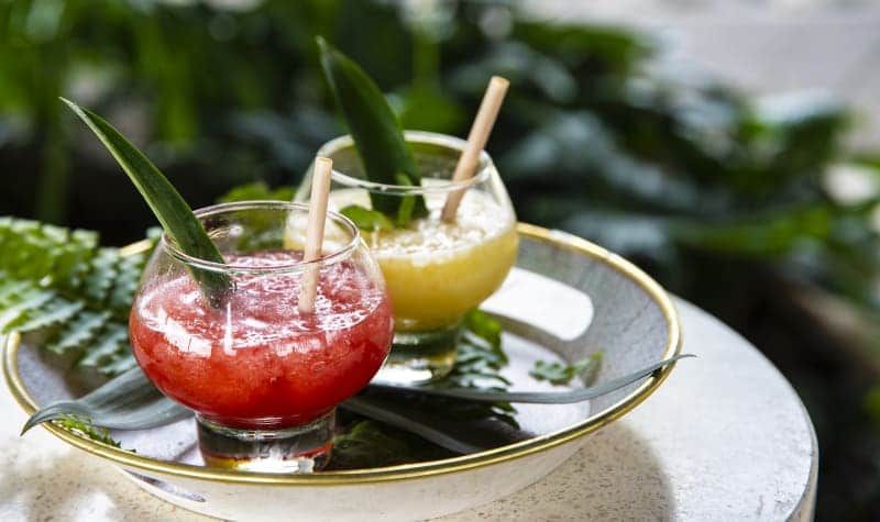 Two drinks in glasses with straws on a plate on a table.