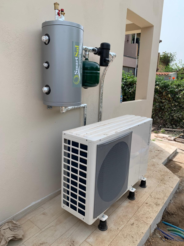 Uno scaldabagno a pompa di calore con serbatoio a parete e una grande unità esterna posizionata su un patio piastrellato.
