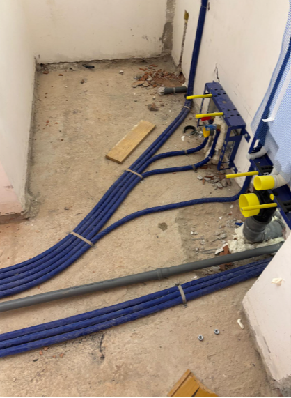 In una stanza non rifinita, dei tubi blu attraversano un pavimento di cemento e conducono alla struttura di installazione di un WC a parete.