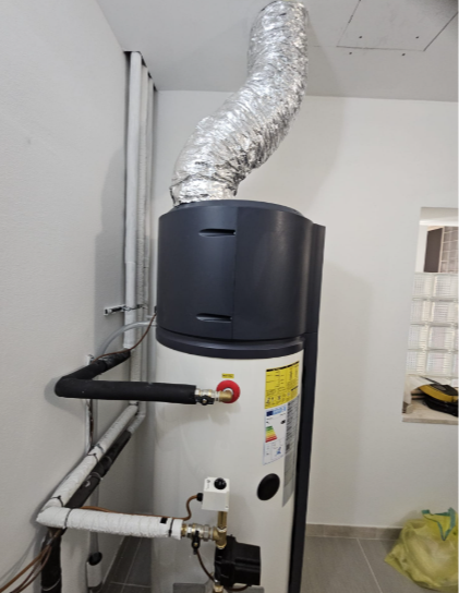 Un serbatoio per le acque grigie, un vaso di espansione verde e tubature installati su una parete accanto a un'unità esterna di condizionamento dell'aria.