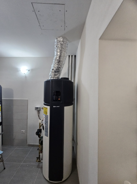 Scaldabagno a pompa di calore bianco e nero con tubo di sfiato flessibile metallico che si estende fino a un pannello di accesso a soffitto.
