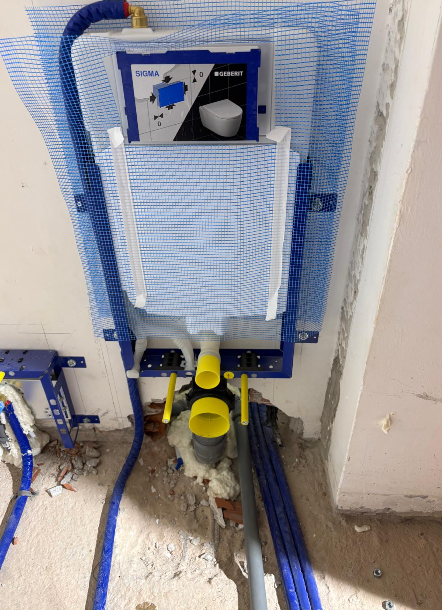 Struttura di installazione per WC a parete con tubature, rete blu e tappi gialli in un cantiere.
