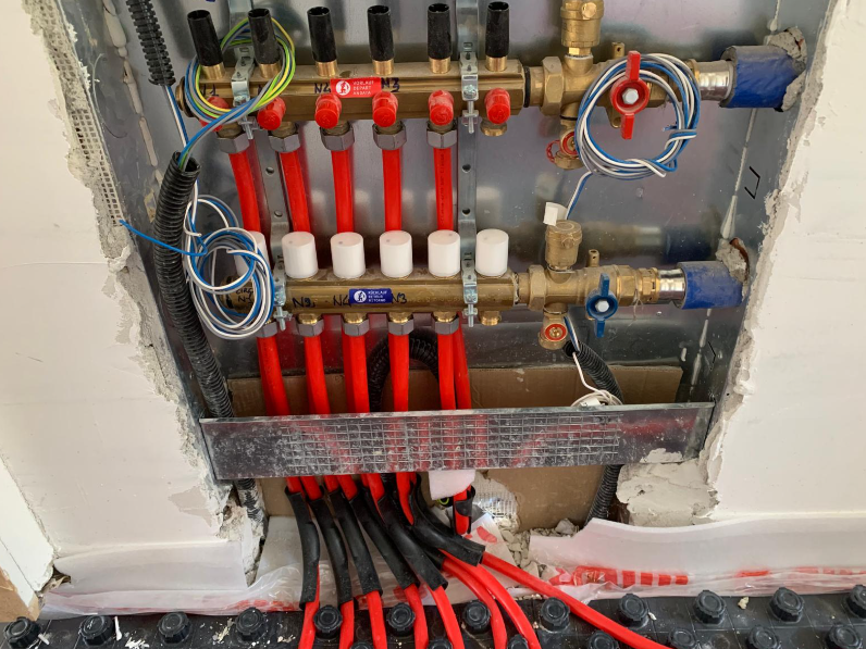 Collettore per riscaldamento a pavimento radiante incassato nella parete, con tubi rossi e valvole bianche montate all'interno di un alloggiamento metallico.