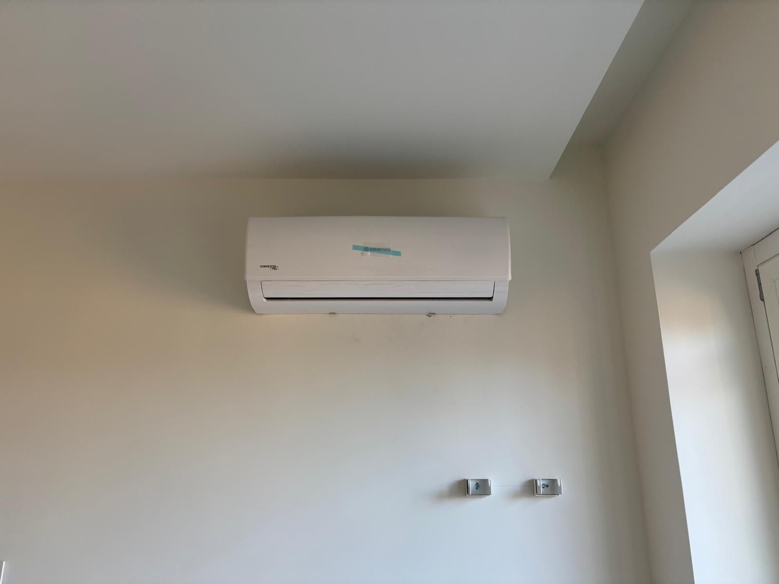 Unità di climatizzazione a soffitto con condotti metallici, tubi grigi e cablaggio elettrico in un corridoio interno non rifinito.