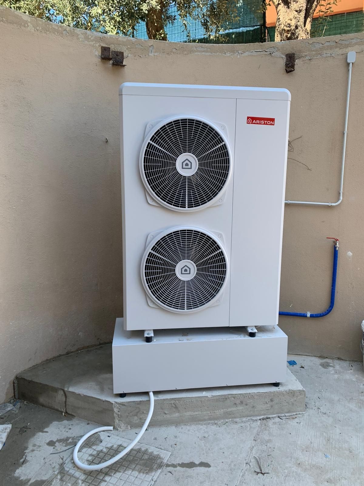 Uno scaldabagno a pompa di calore bianco con parte superiore nera e condotto di ventilazione argentato installato in un locale di servizio.