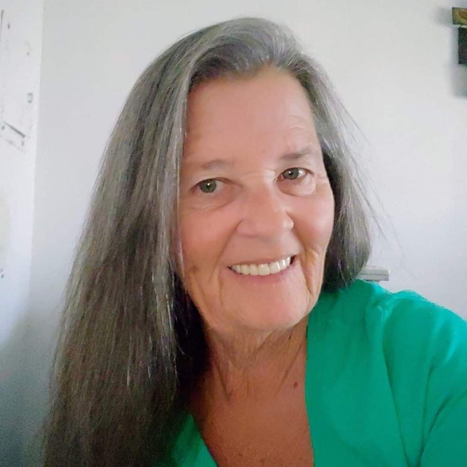 A woman with long gray hair is smiling and wearing a green shirt.