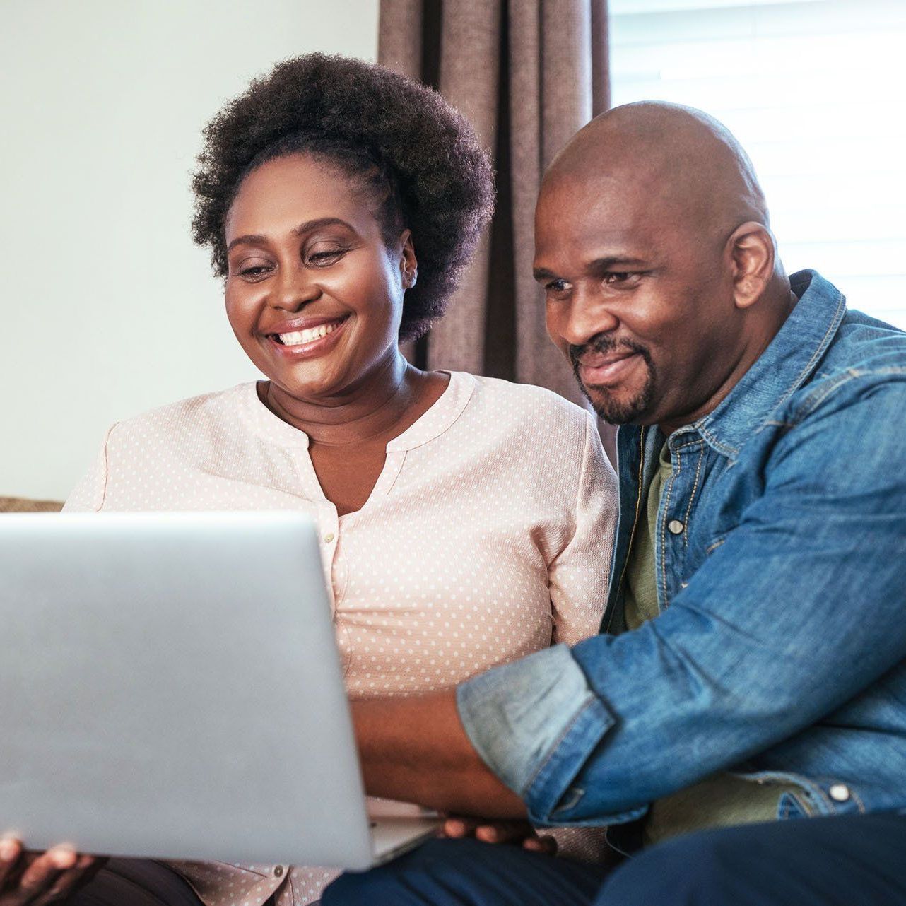 A man and a woman are sitting on a couch looking at a laptop computer.