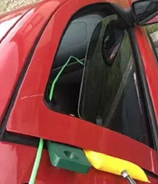 Red car window with green strap and water container attached, possibly for cleaning.