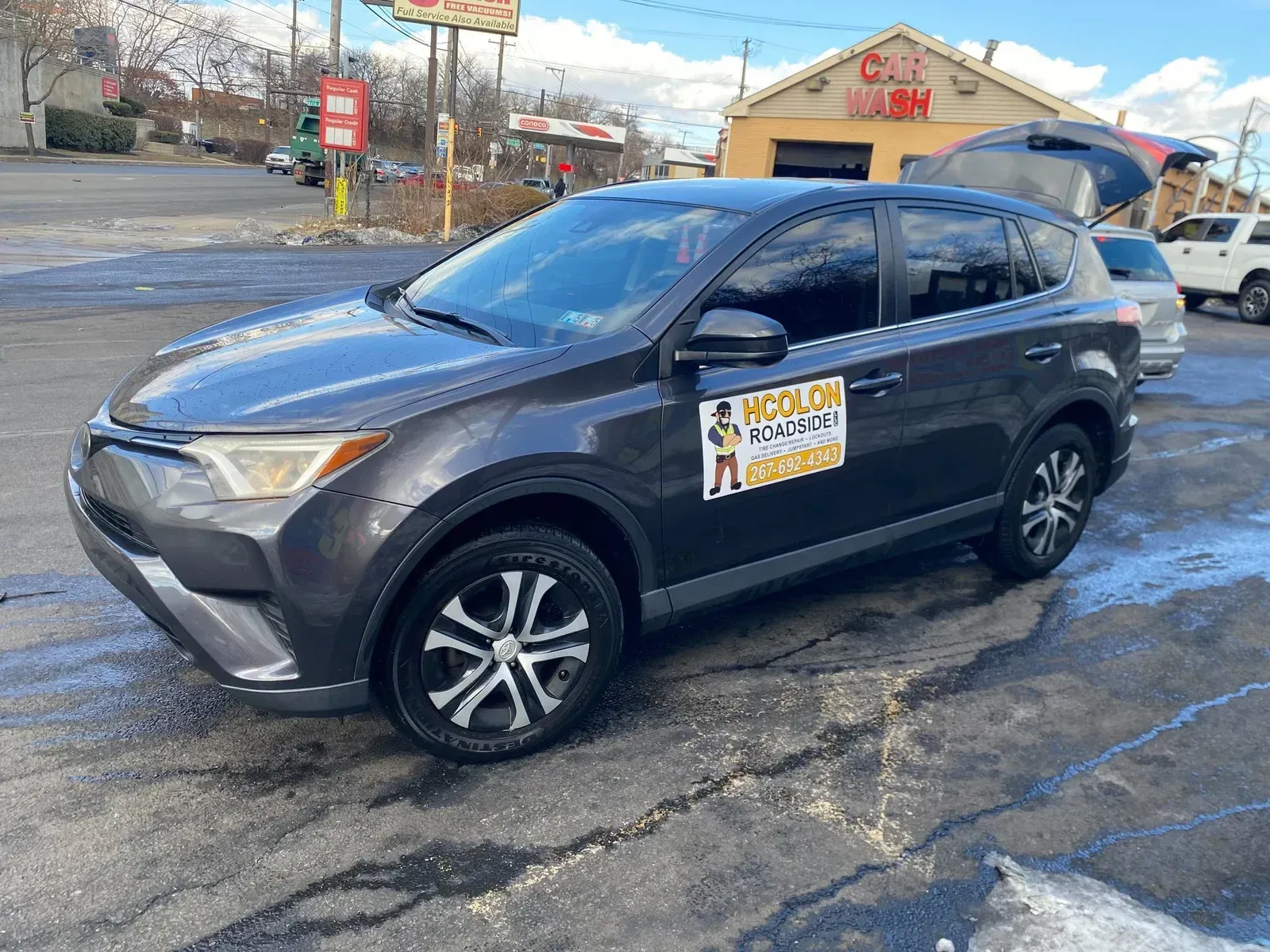 Dark gray SUV with logo parked outside a car wash on a sunny day.