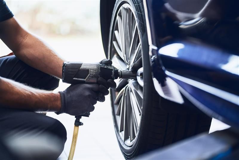 Mechanic uses an impact wrench to remove a wheel from a blue car.