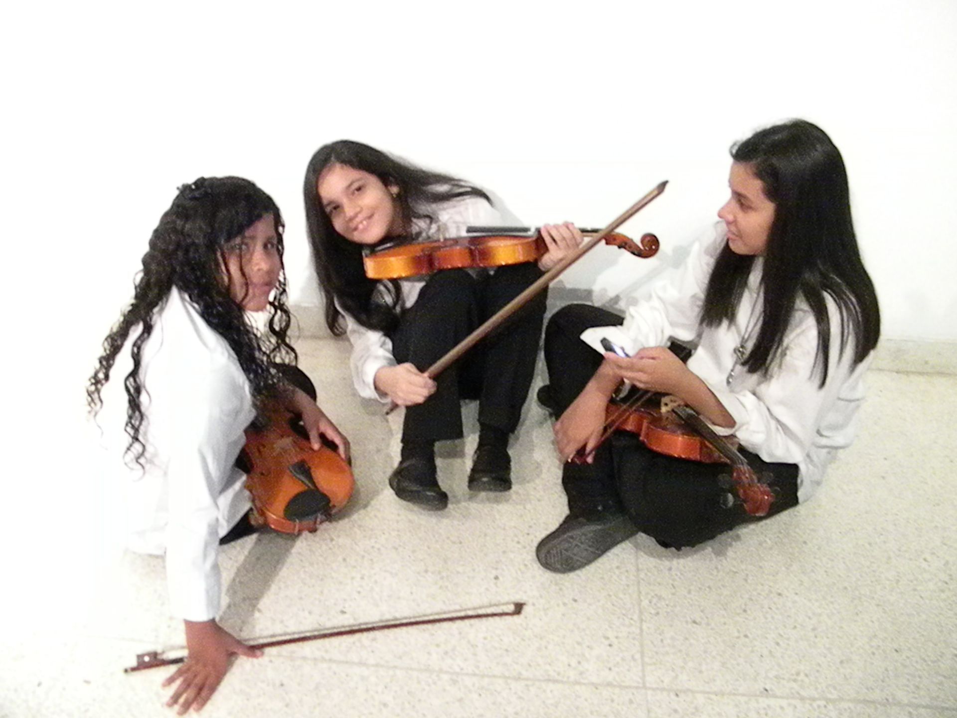 Three girls are sitting on the floor playing violins