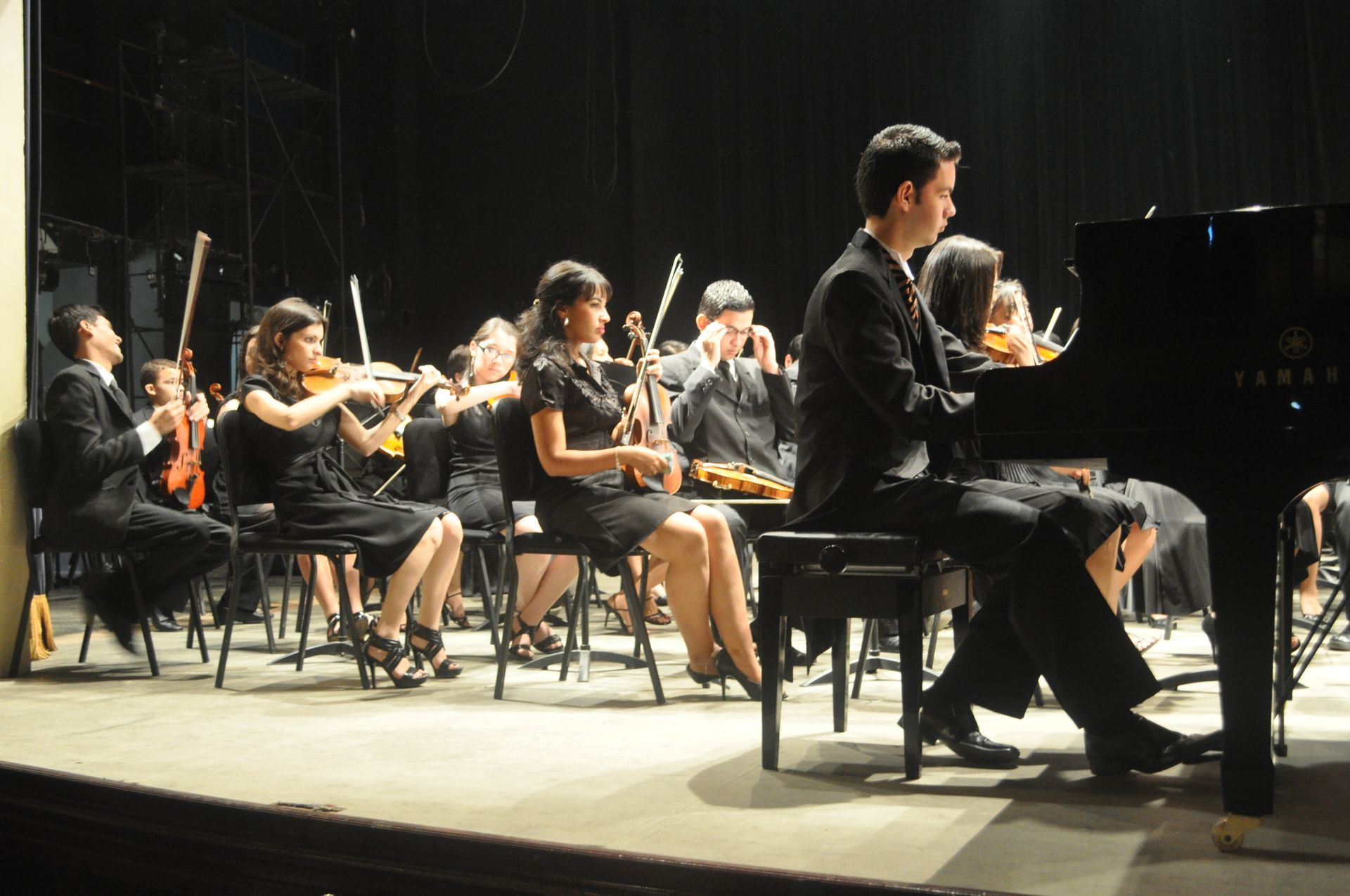 A man is playing a piano in front of an orchestra