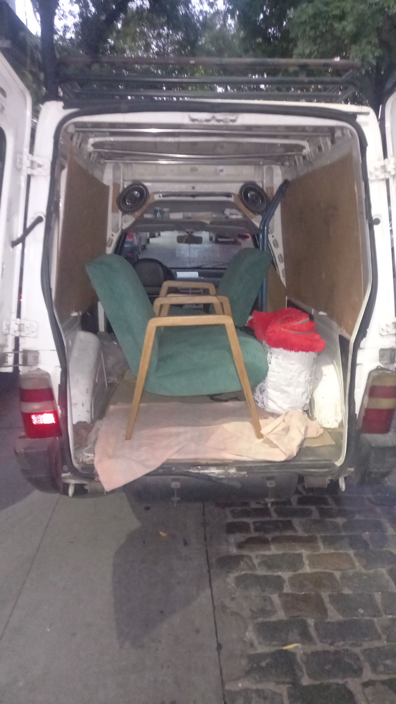 Furgoneta abierta con una silla verde, un taburete de madera y diversos artículos en su interior.