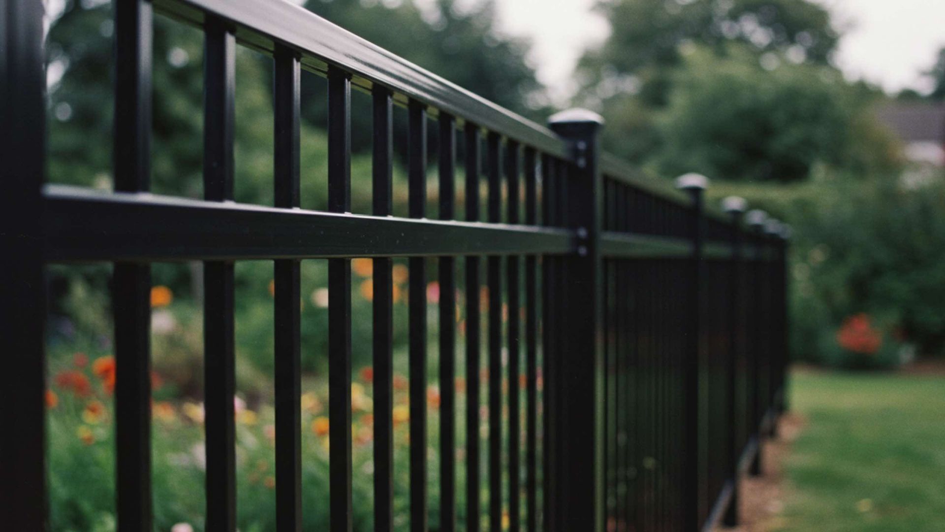Black metal fence in a garden, with flowers and greenery visible in the background.