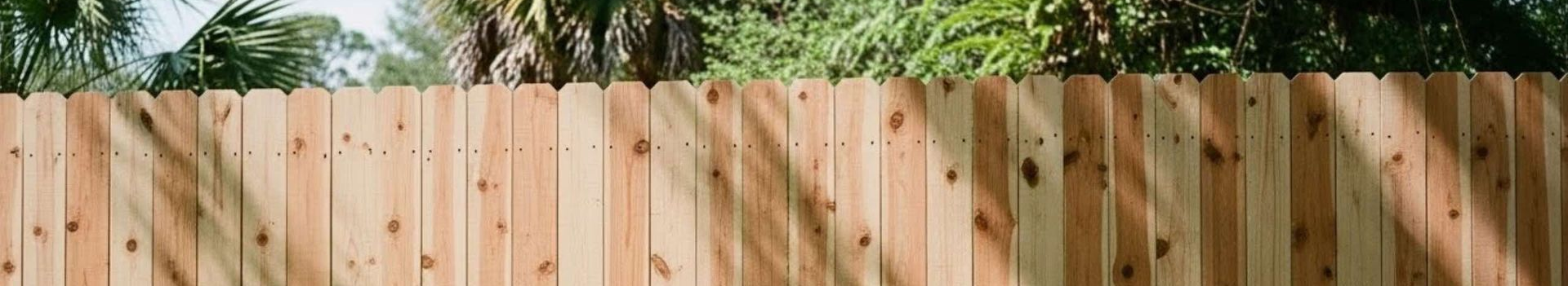 Wooden privacy fence with shadows and green grass.