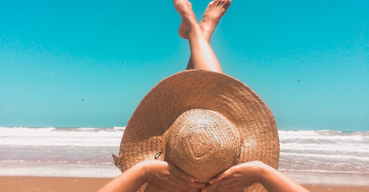 A woman is laying on the beach wearing a straw hat.