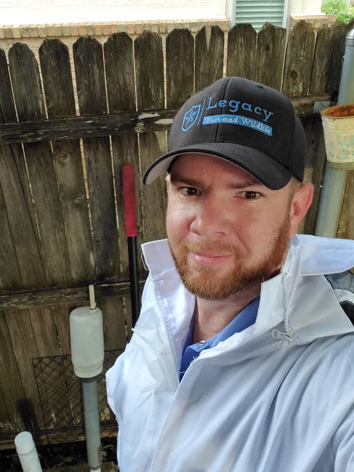 A man wearing a hat and a white jacket is standing in front of a wooden fence.