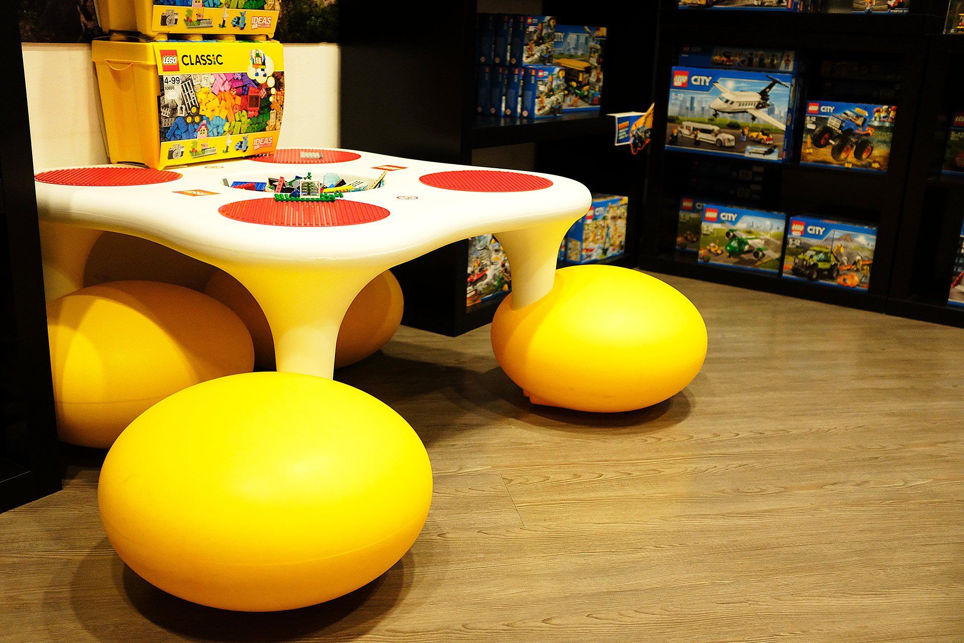 Un tavolo per bambini con pouf gialli in una stanza piena di giocattoli Lego.