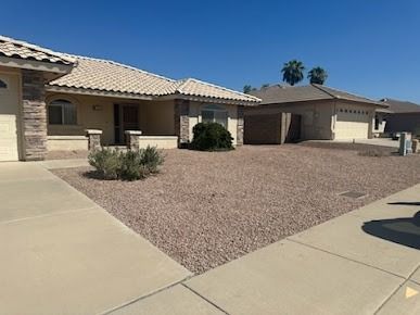 Tan house with gravel yard, shrubs, and sidewalk under a blue sky.