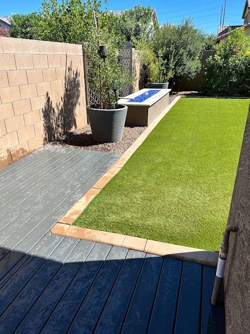 Backyard with gray deck, artificial green lawn, and a fire pit.