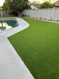 Green artificial lawn bordering a pool, set against a white wall and houses.