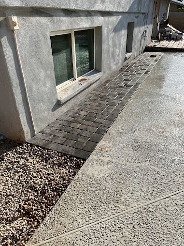 Exterior view of a building's foundation with a brick walkway, gravel, and concrete patio.