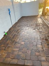 Brick paved area next to a white wall, with a hose and some plants.