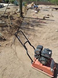 A soil compactor in front of a construction site; a person works in the background.