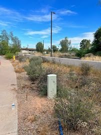 Pathway along dry vegetation; gray wall, utility box, blue sky.