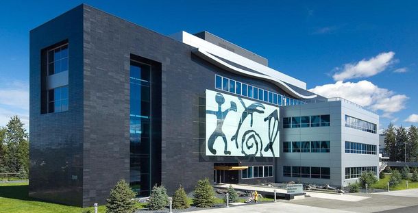 Modern, dark-gray building with abstract art on the facade under a clear, blue sky.