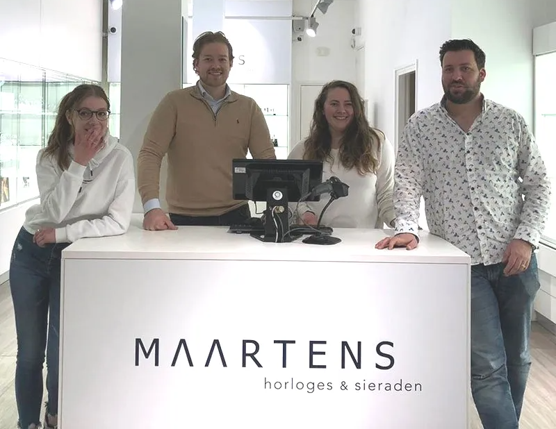 Eine Gruppe von Menschen steht um einen Tresen herum, auf dem Maartens steht