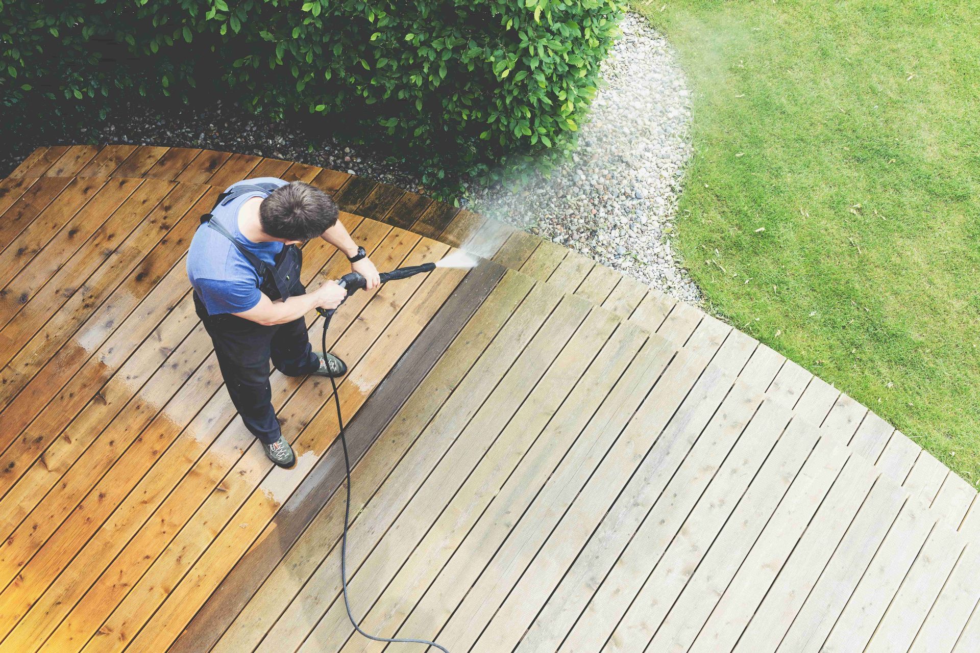 Man power washing a wooden deck in a backyard, water spraying.
