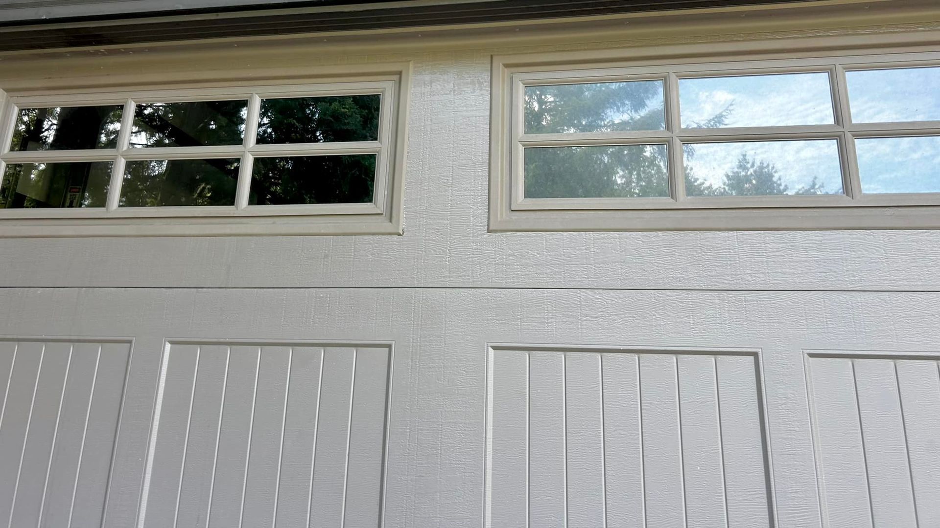 A close-up view of the upper panels of a light-colored, textured garage door with two rectangular, grid-style windows.
