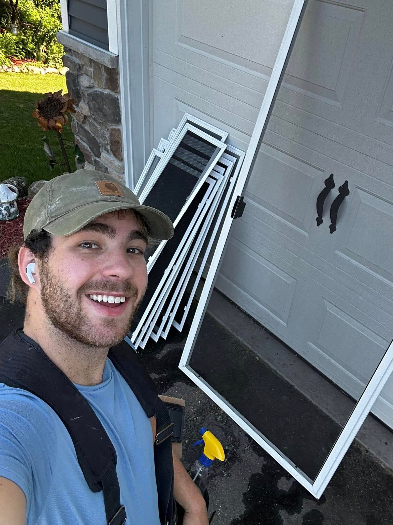 Man smiles at the camera, holding screen window frames near a garage door.