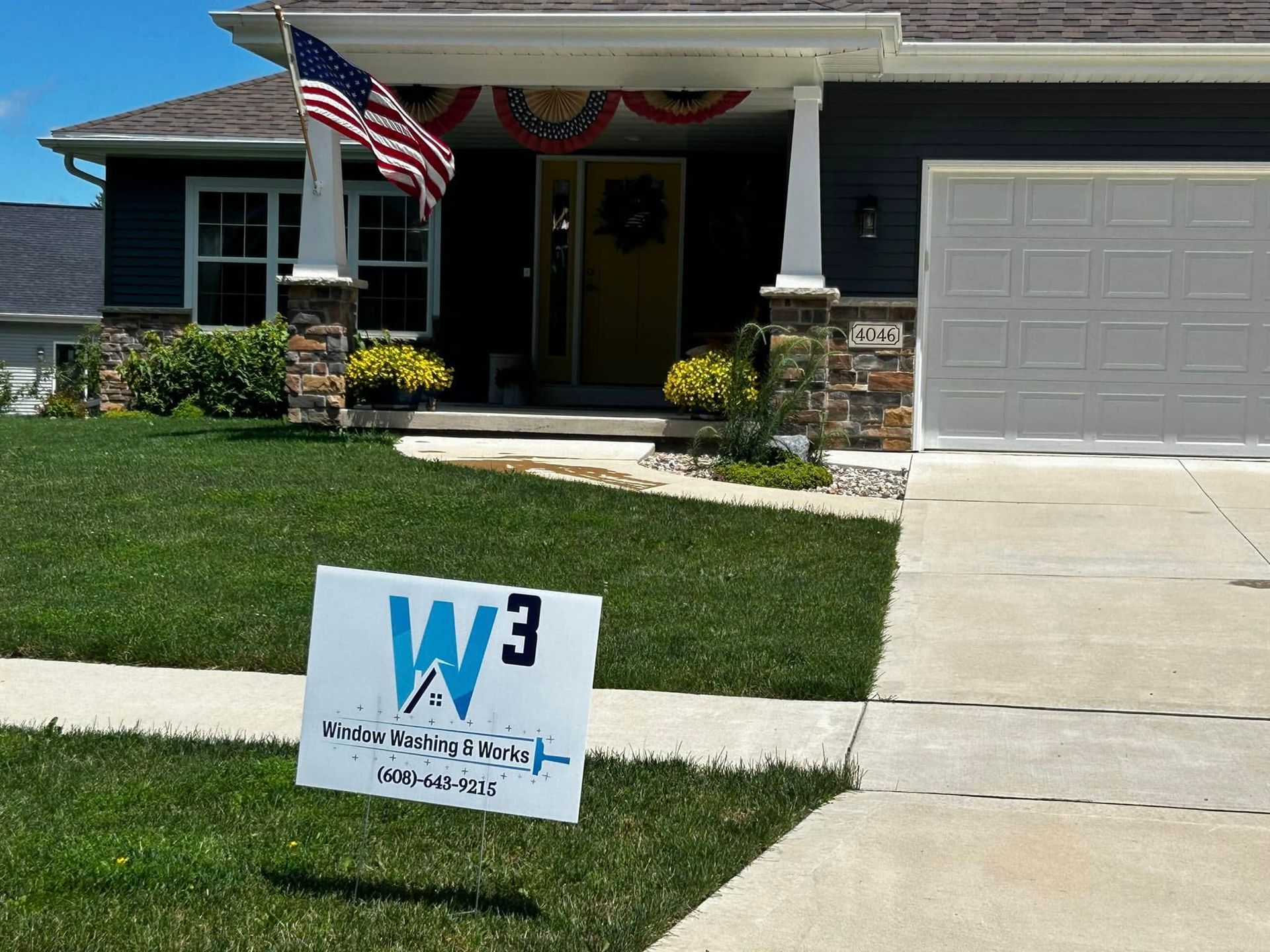 A house exterior with dark siding, stone accents, a lawn, and a sign for W3 Home Improvements in the foreground.