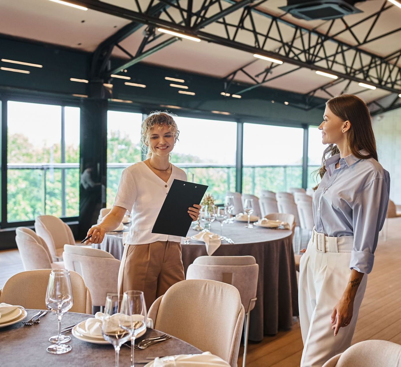 A restaurant employee is guiding a guest to a table next to the window based on her reservations and profiles on Front Reserve.