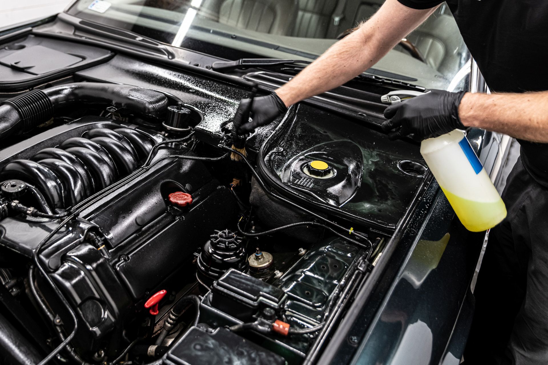 Person cleaning a car engine, spraying a yellow liquid with black gloves.