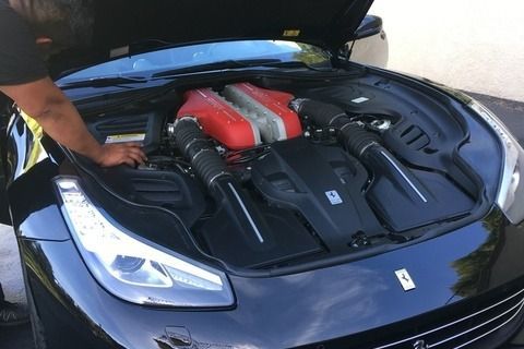 Black Ferrari with open hood, engine visible, being inspected.