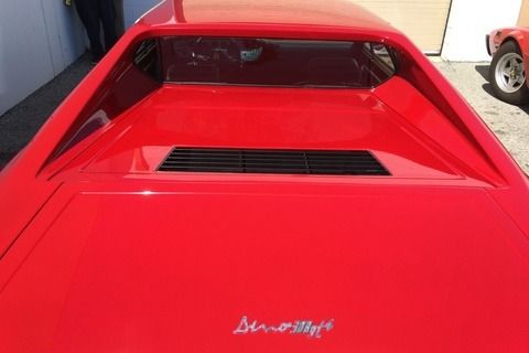 Red car, rear view. Rectangular vent and Dino silhouette logo visible.