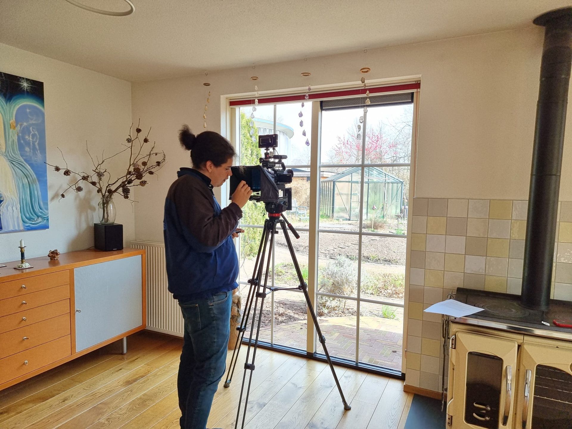 Een vrouw staat voor een camera op een statief in een woonkamer