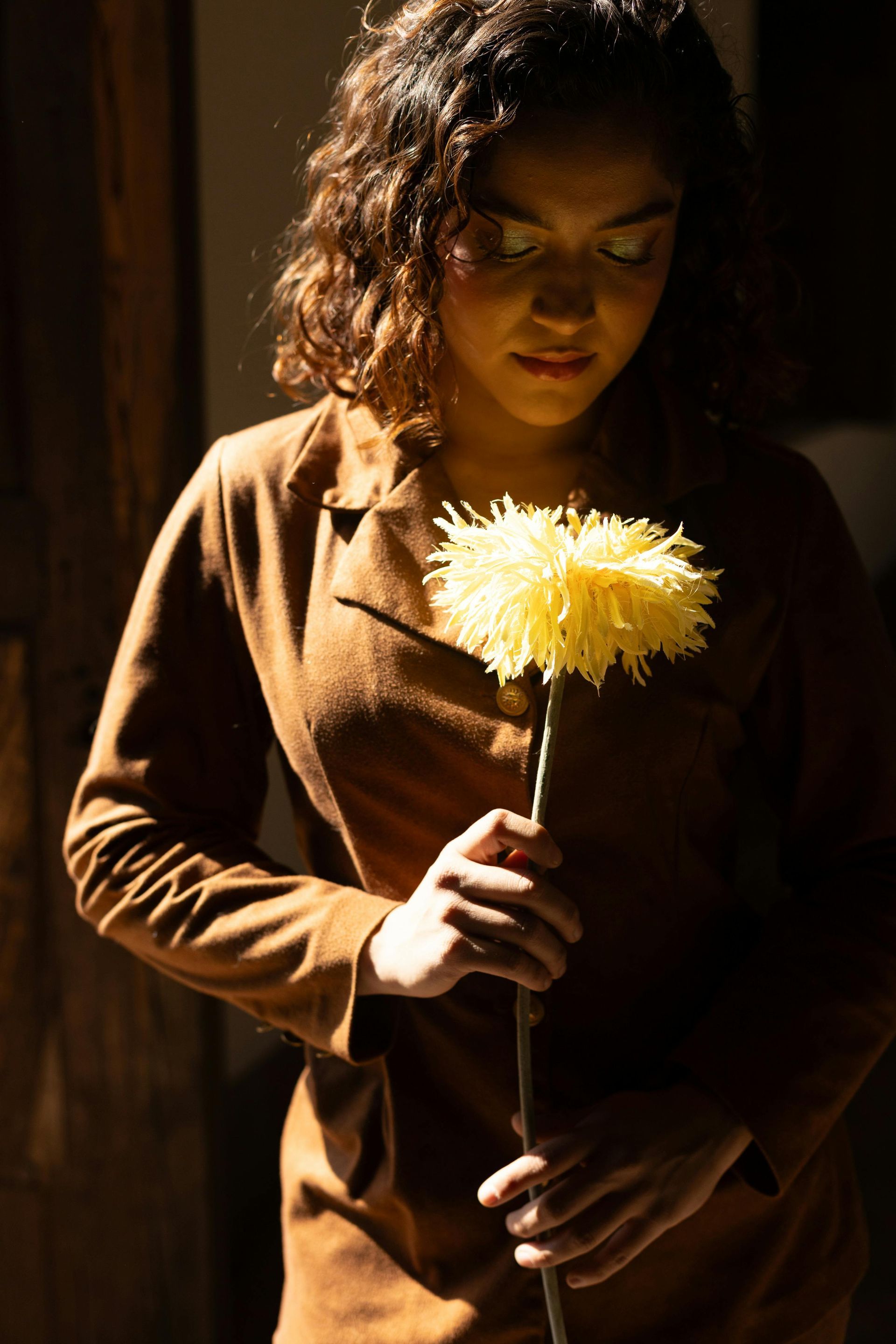 Een vrouw in een bruine jurk houdt een gele bloem vast.