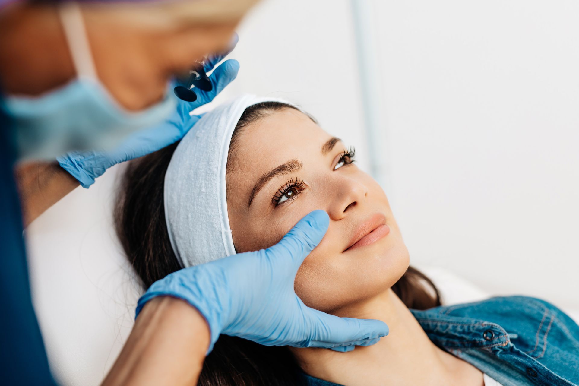 Person wearing blue gloves examining jawline during a cosmetic procedure.