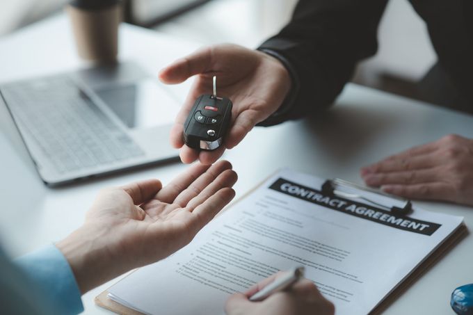 Un uomo consegna le chiavi dell'auto a un altro uomo mentre firma un contratto.