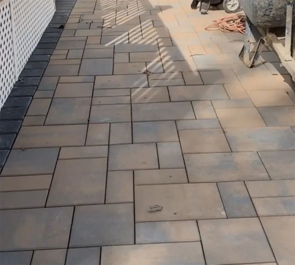 Paver patio with a white fence on the left and a cement mixer on the right.