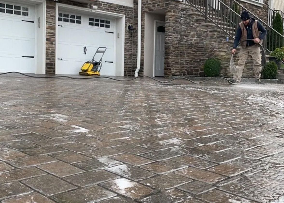 Man pressure washing a brick driveway near a house with white garage doors.