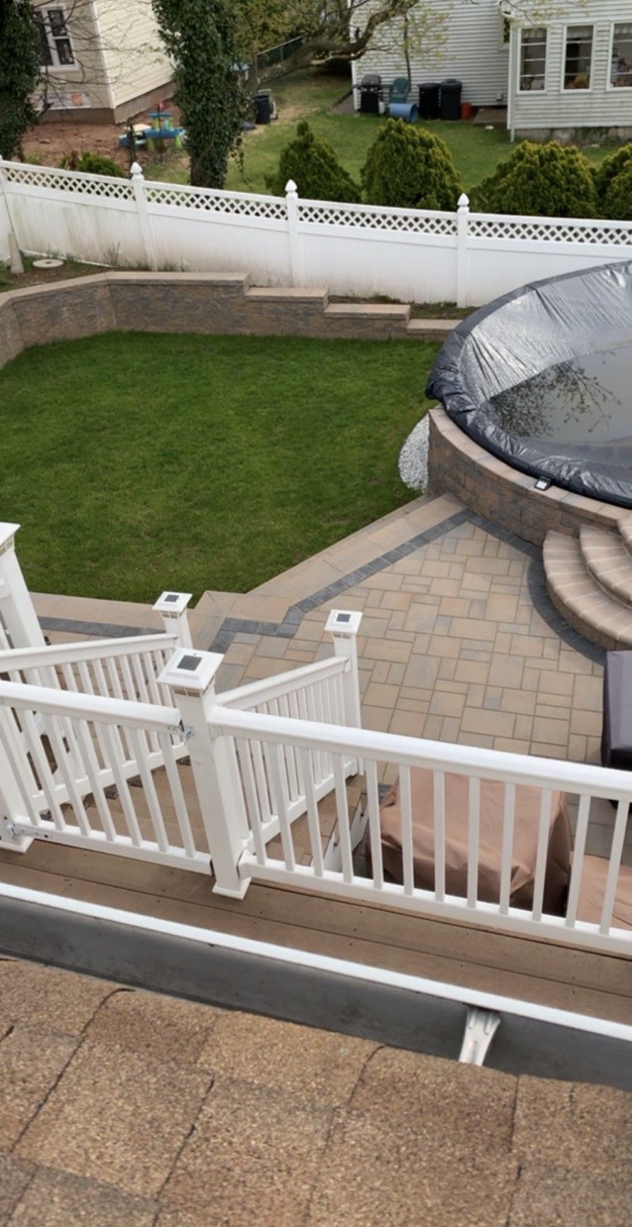 A backyard patio with a pool, stairs, lawn, and white railing.
