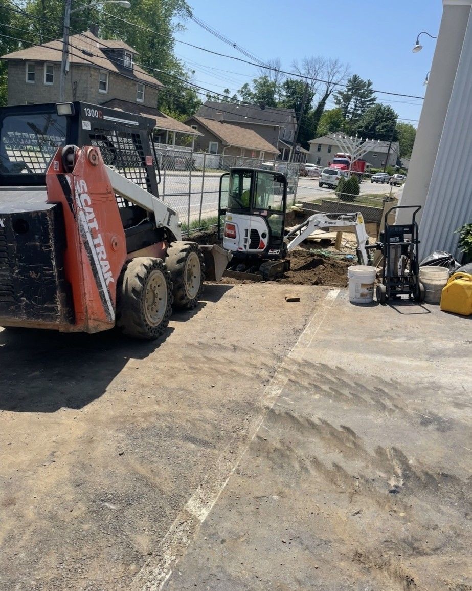 Construction site with Bobcat skid steer and mini excavator. Excavation in progress, concrete area.