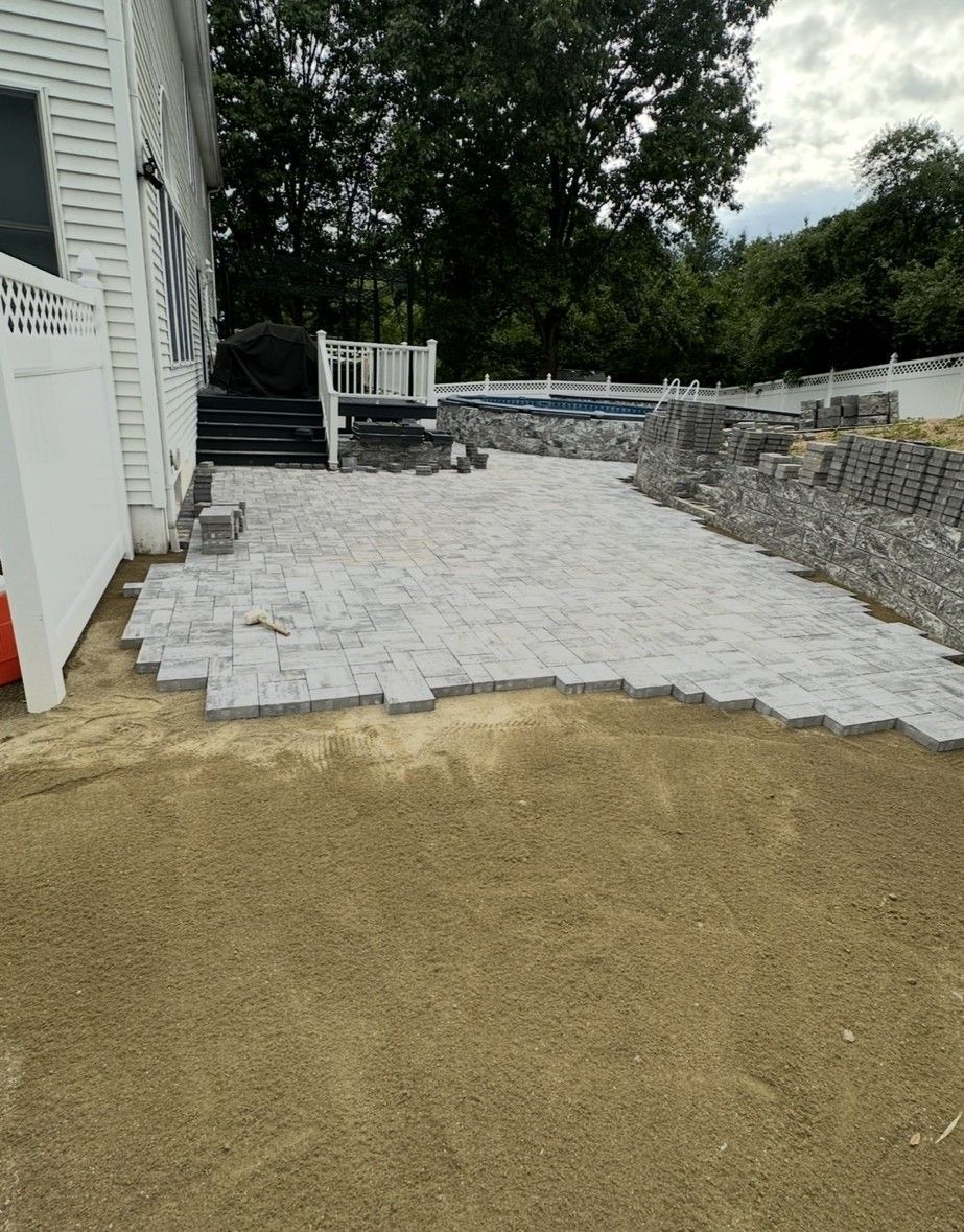 Backyard patio under construction with gray paving stones and landscaping materials.